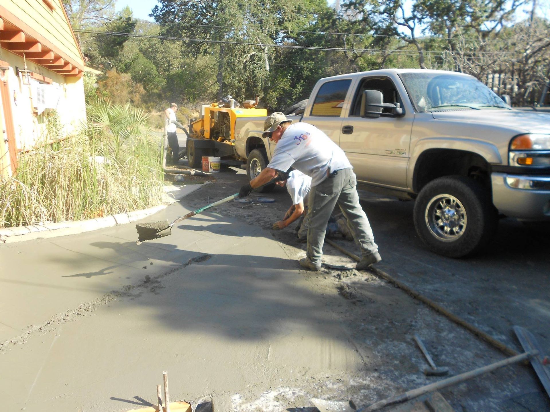 Road repair crew pouring fresh concrete beside a silver pickup truck on a curved driveway