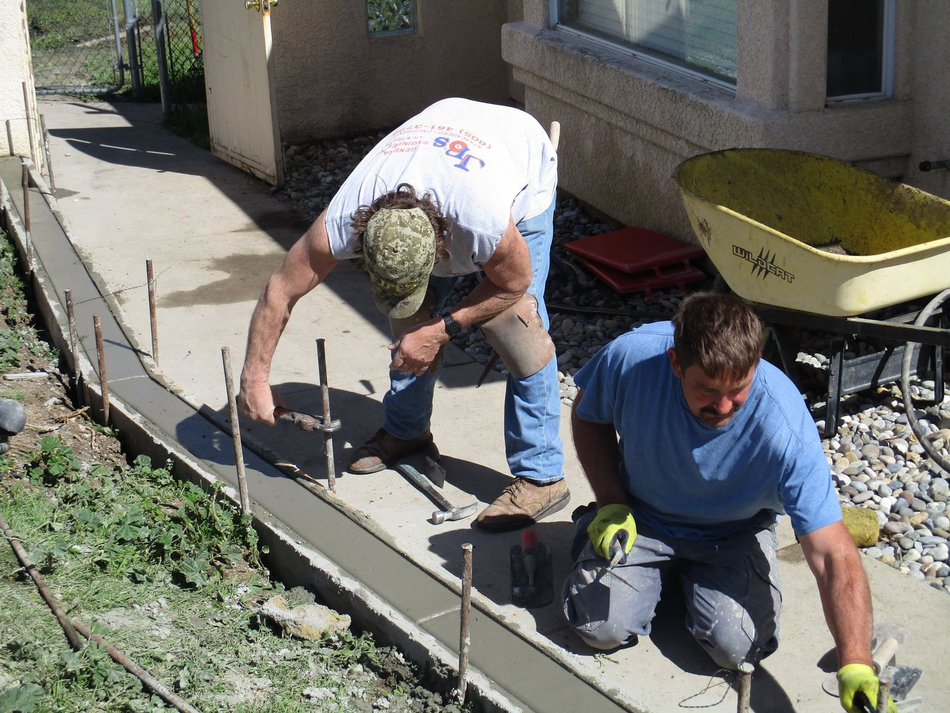Two workers pouring and smoothing concrete along a house foundation