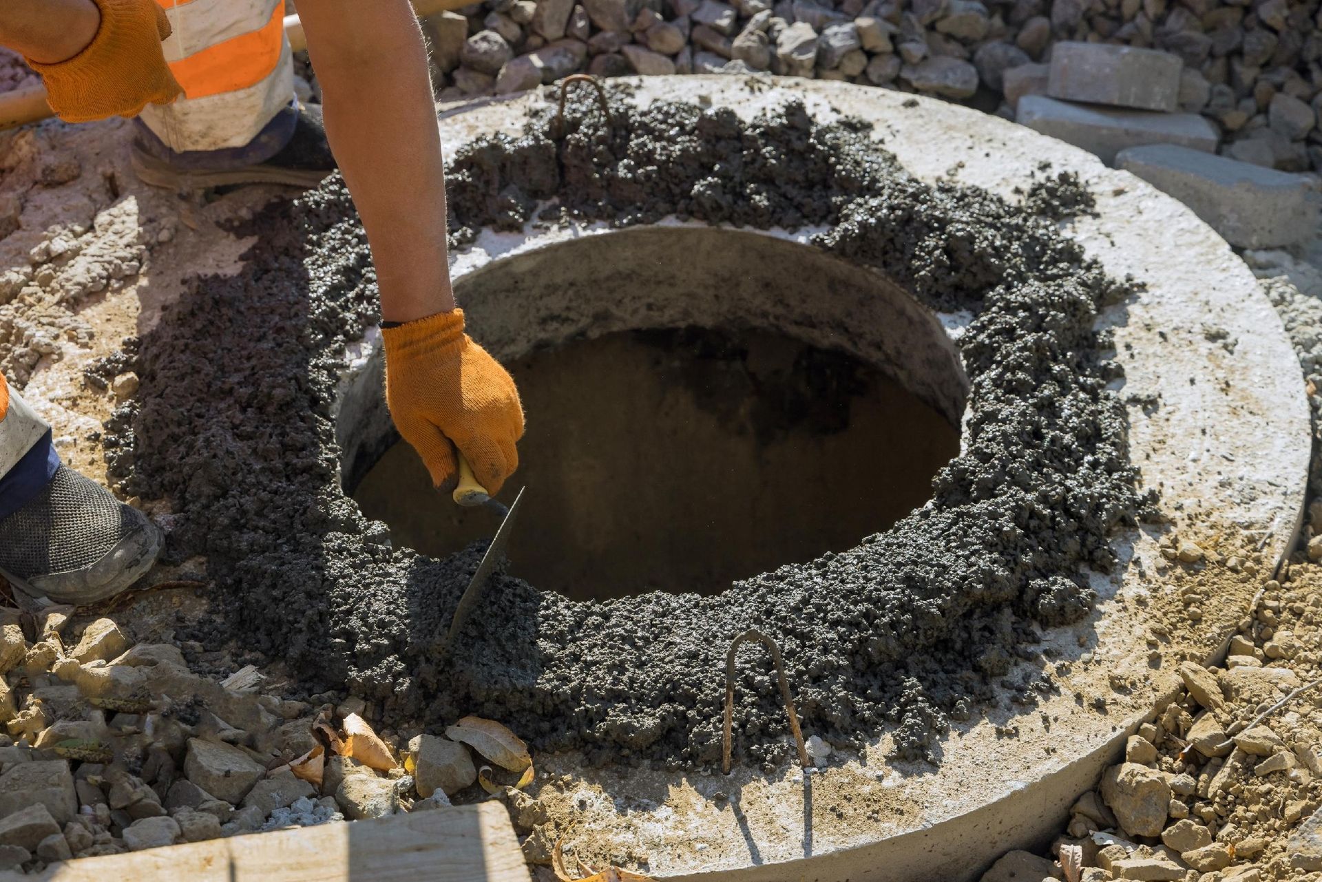 Gloved worker smoothing wet concrete around a circular manhole opening at a construction site