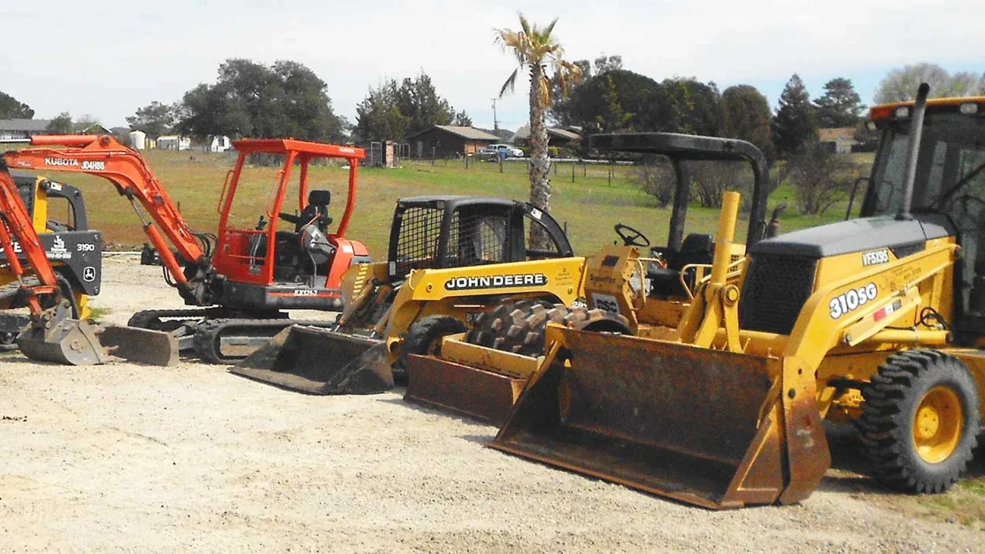 Row of yellow and orange construction loaders parked on gravel outdoors