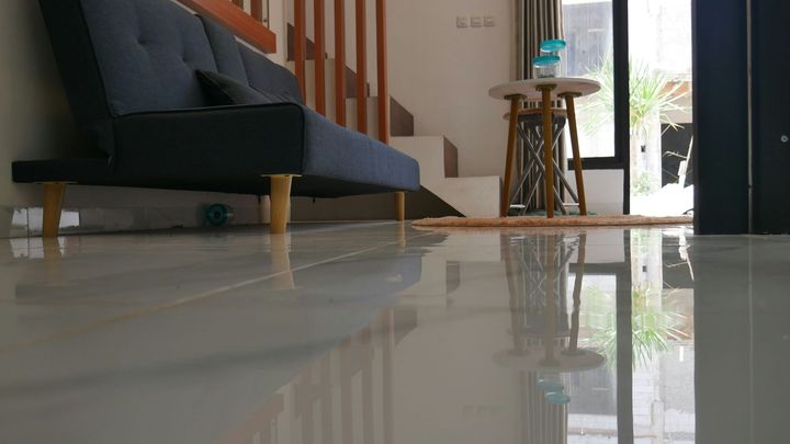 Living room with a black sofa, wooden side table, and glossy tiled floor reflecting the furniture and window light
