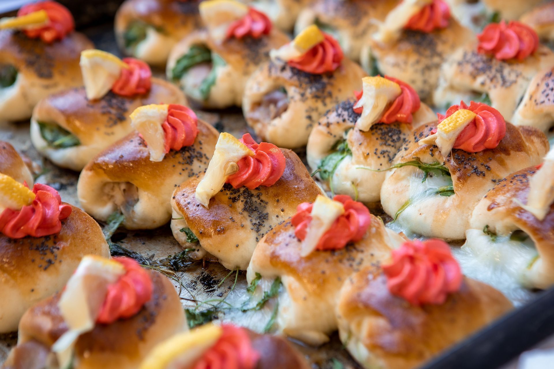 Vassoio di pasticcini cotti al forno, dorati, ricoperti di glassa rossa e spicchi di limone.