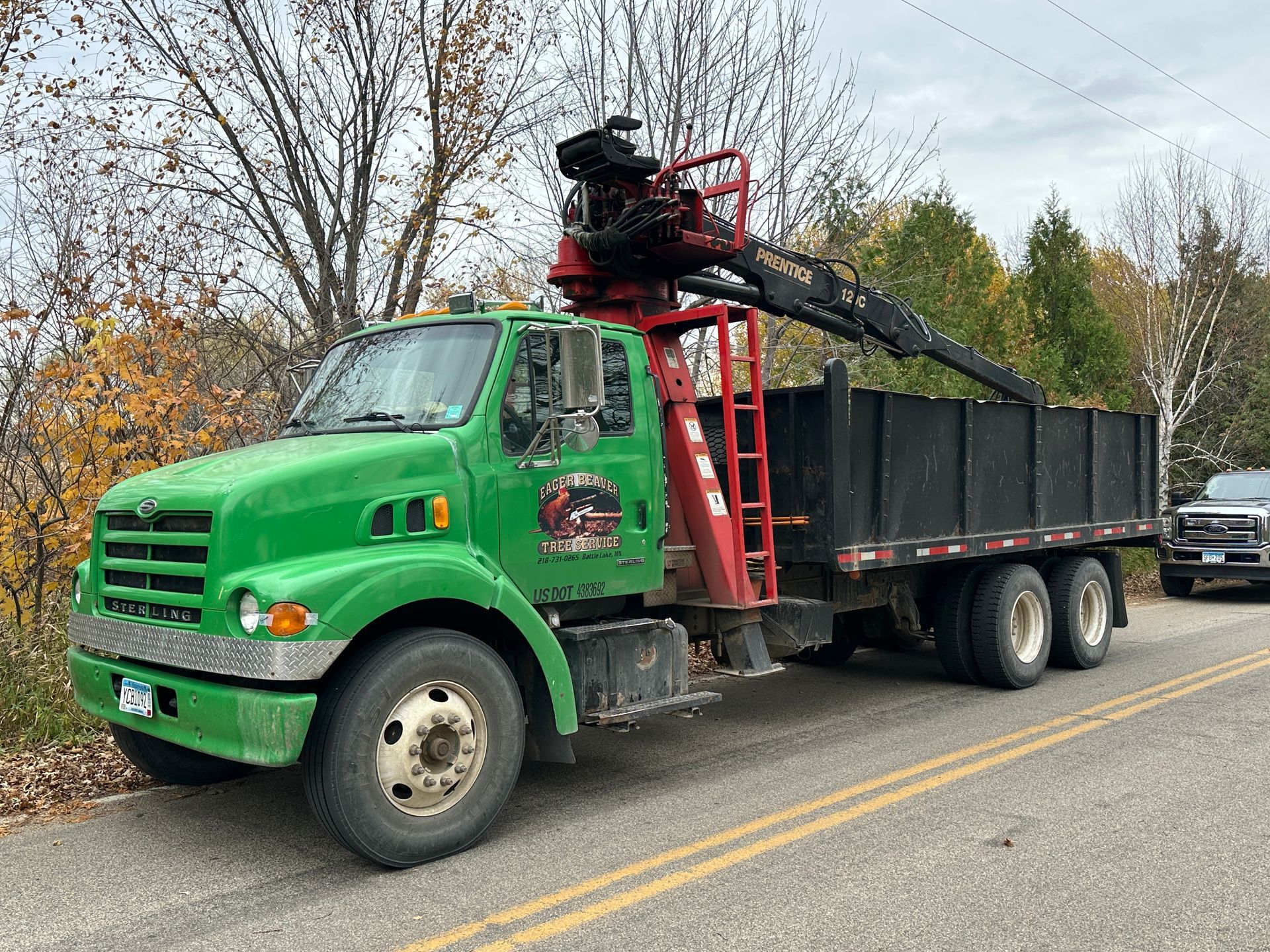 Green truck with crane and dump bed on side of road. Green truck with crane and dump bed on side of road.
