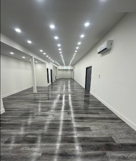 Empty, modern, long room with wood-look flooring, white walls, and recessed lights. Includes a/c unit and doorways.