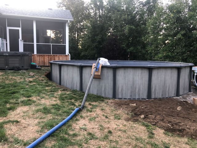 A gray, circular above-ground pool sits in a grassy yard next to a screened porch, with a blue drainage hose attached.