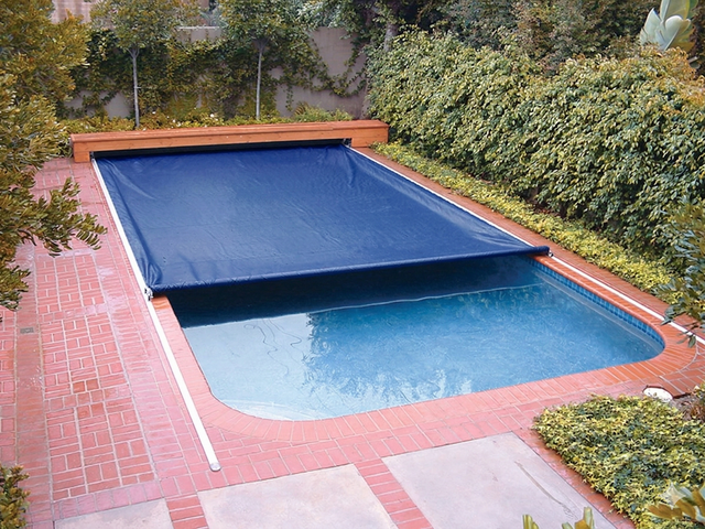 A rectangular backyard swimming pool partially covered by a dark blue automatic retractable cover.