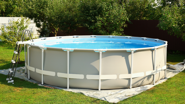 A round, grey, above-ground swimming pool with a metal frame and an attached ladder, sitting on a lawn in a yard.
