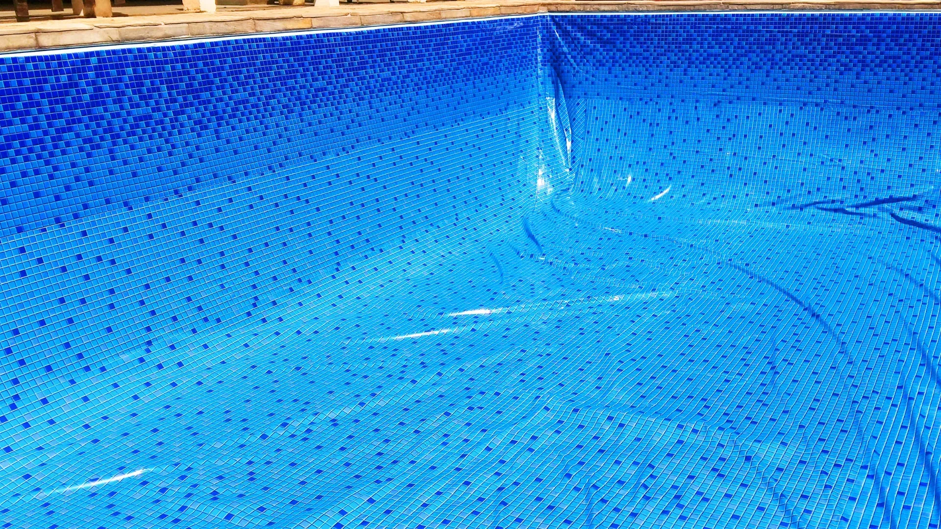 A blue solar pool cover floats on the water in the corner of a rectangular swimming pool.