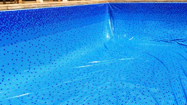 A blue solar pool cover floats on the water in the corner of a rectangular swimming pool.