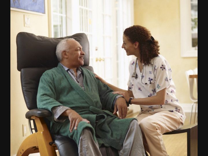 A nurse is talking to an elderly man in a chair