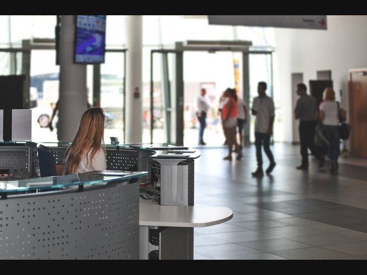 A woman sits at a desk in a busy lobby