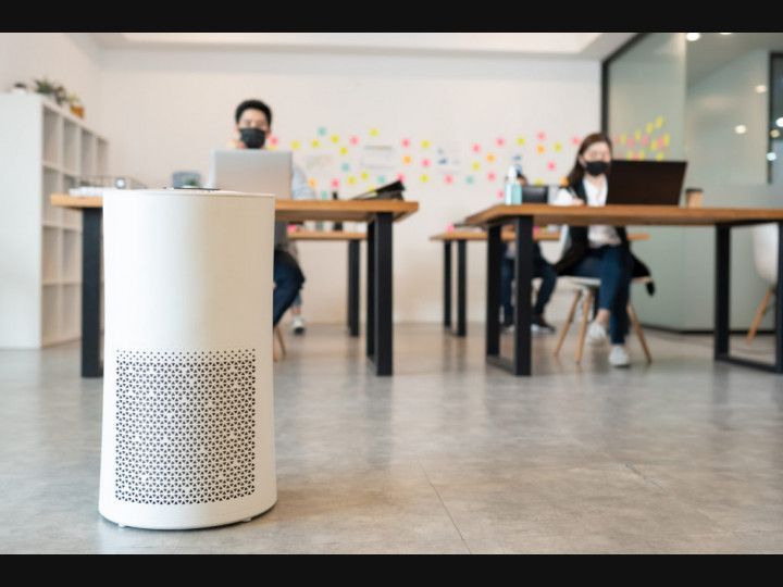 Air purifier is sitting in the middle of an office with people sitting at desks
