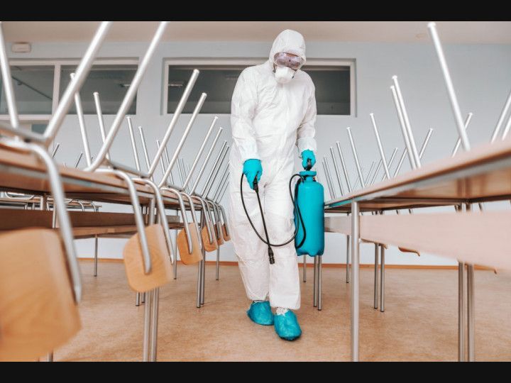 A man in a protective suit is disinfecting a classroom