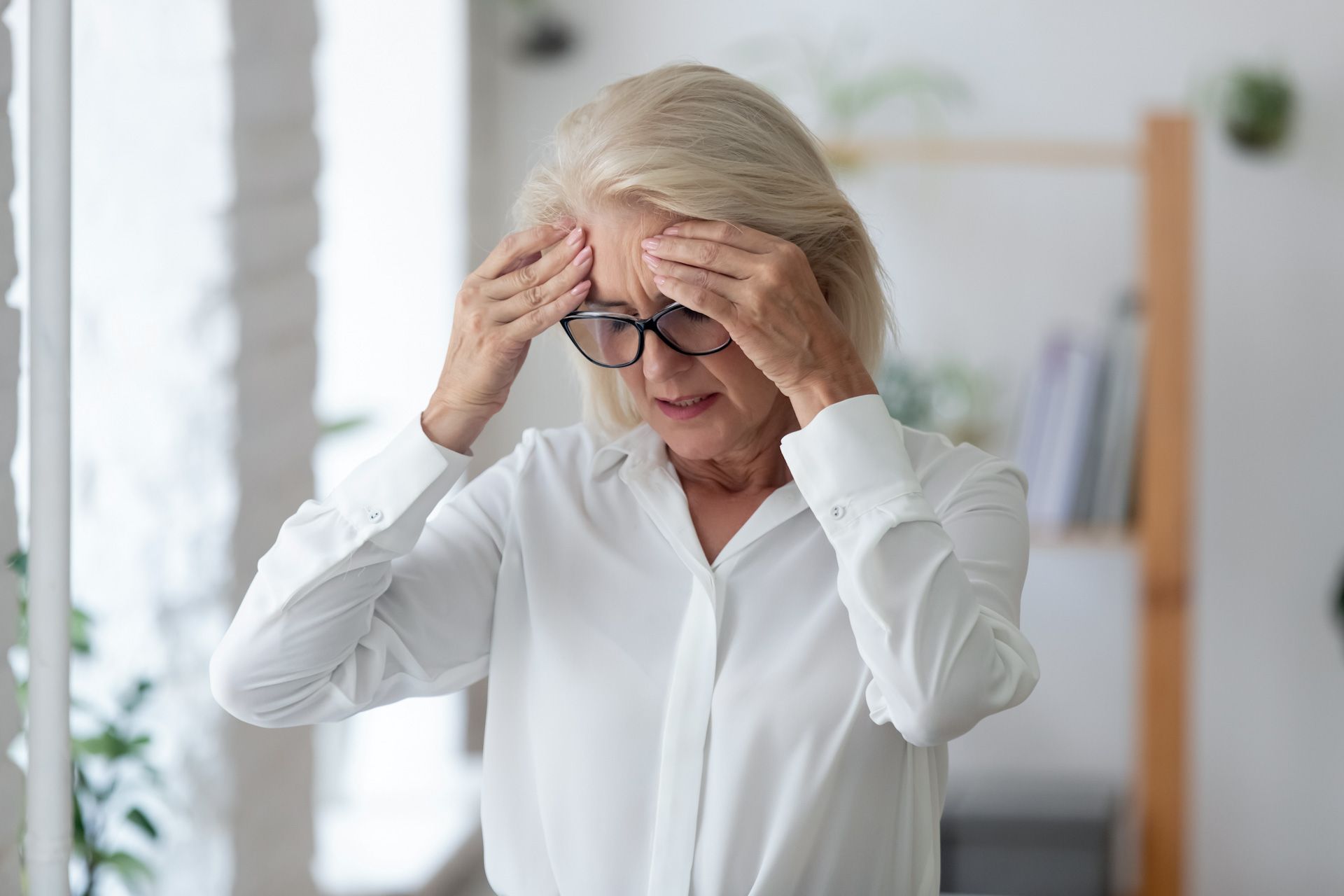 A woman with glasses is holding her head in pain