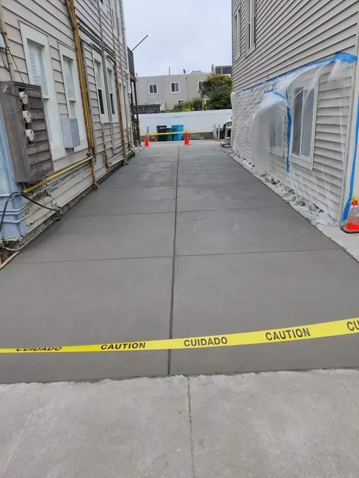 Newly poured concrete pathway between two buildings, blocked by caution tape.