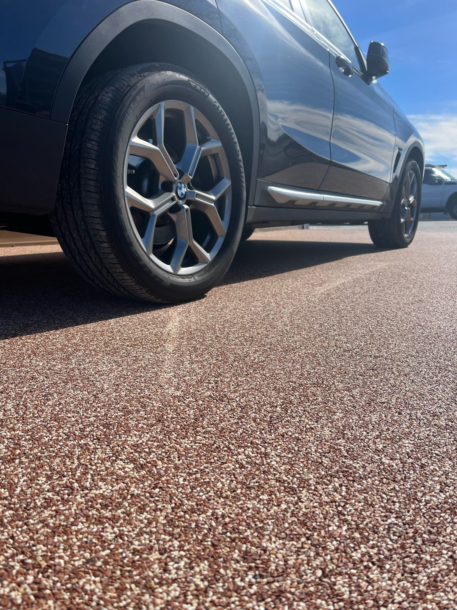 Black SUV parked on a textured reddish-brown surface with a sunny sky background.