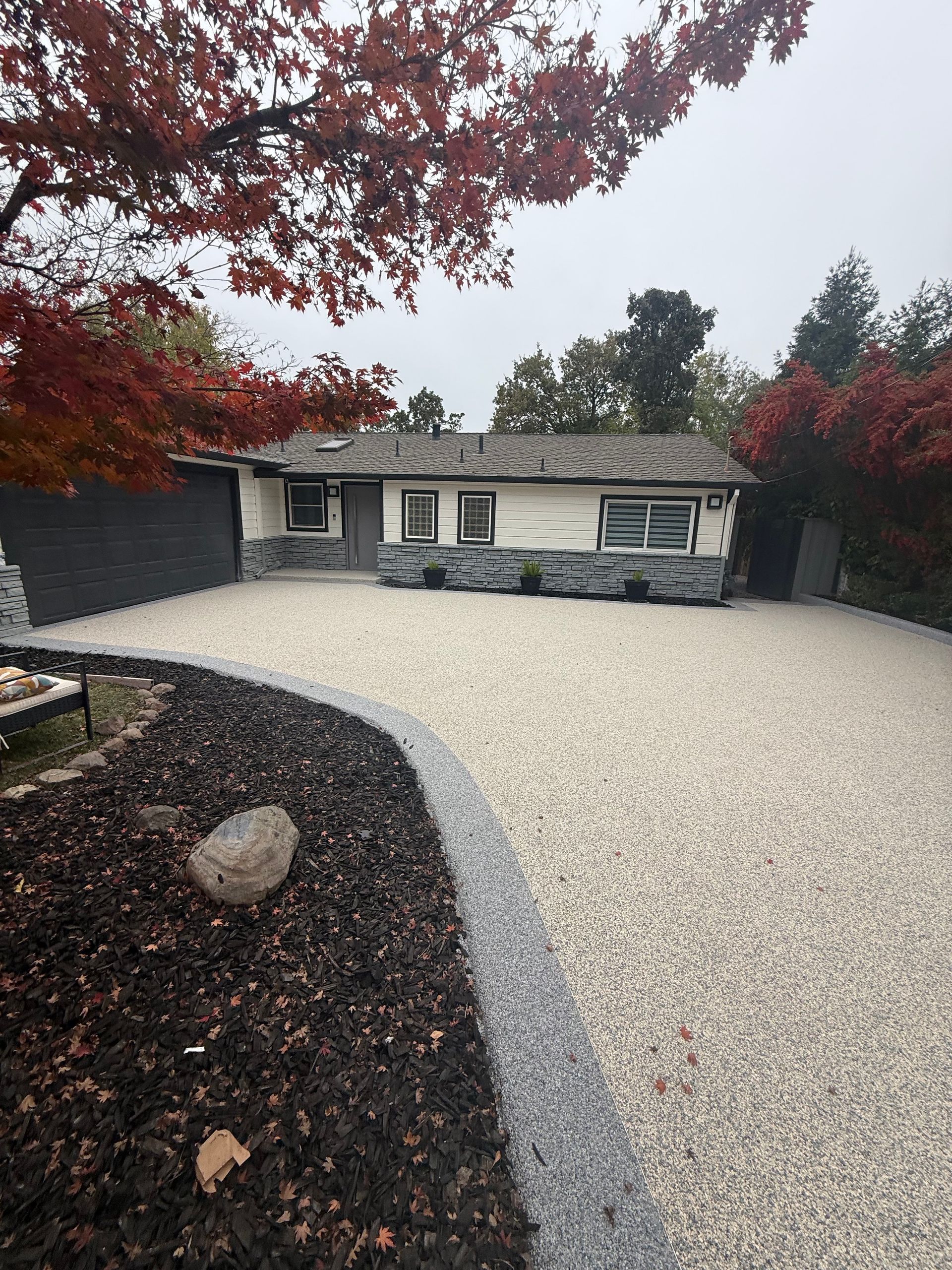 House with gravel driveway, red-leafed tree, and stone accents. Overcast sky.