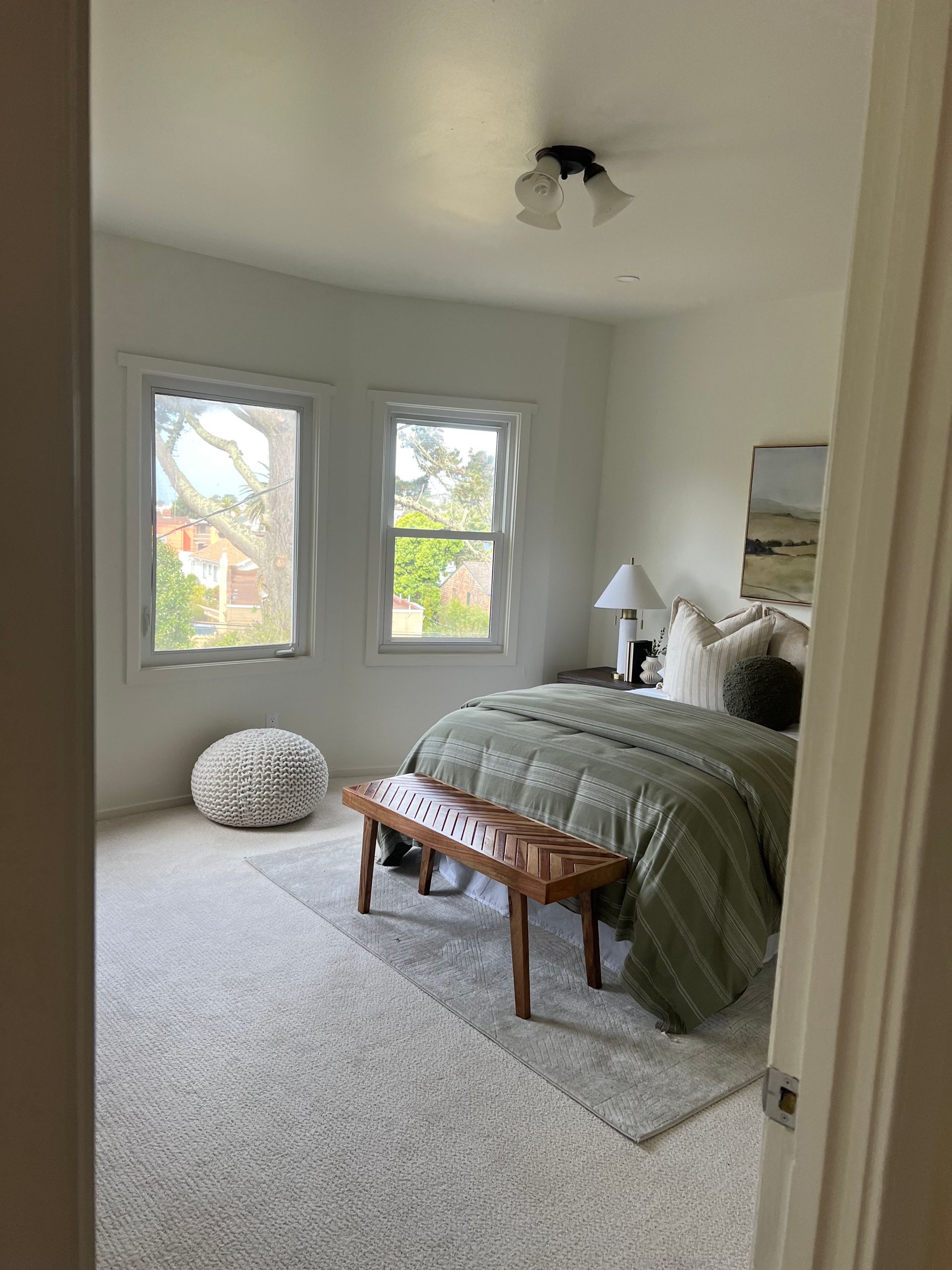 A bedroom with a bed , bench , and two windows.
