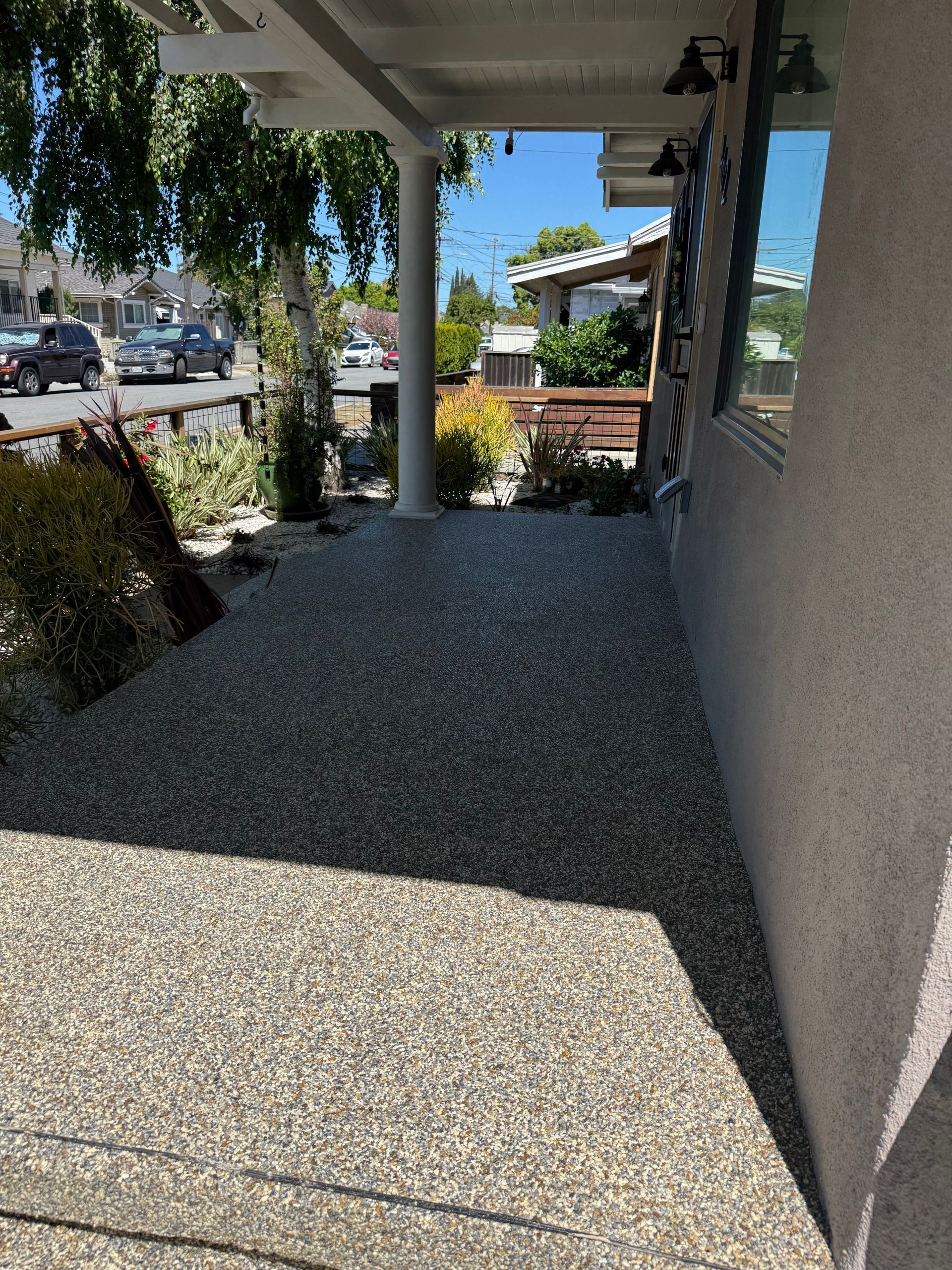 Covered front porch with gravel floor, white columns, and street view beyond the railing.