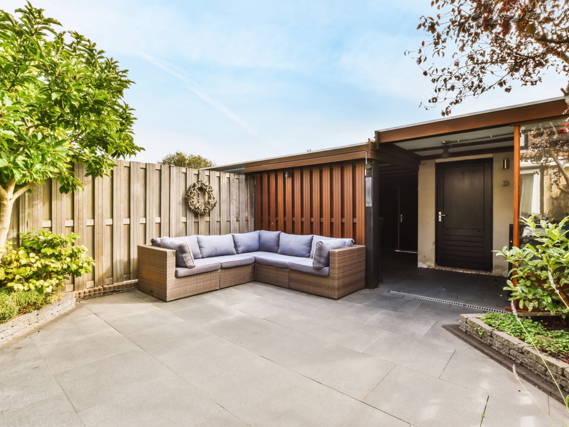 A patio with a sectional couch in front of a house.