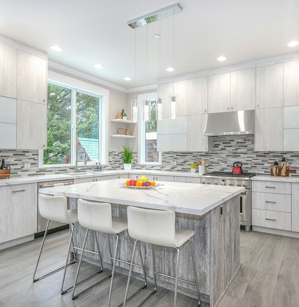 A kitchen with white cabinets , stainless steel appliances , a large island with a table and chairs.