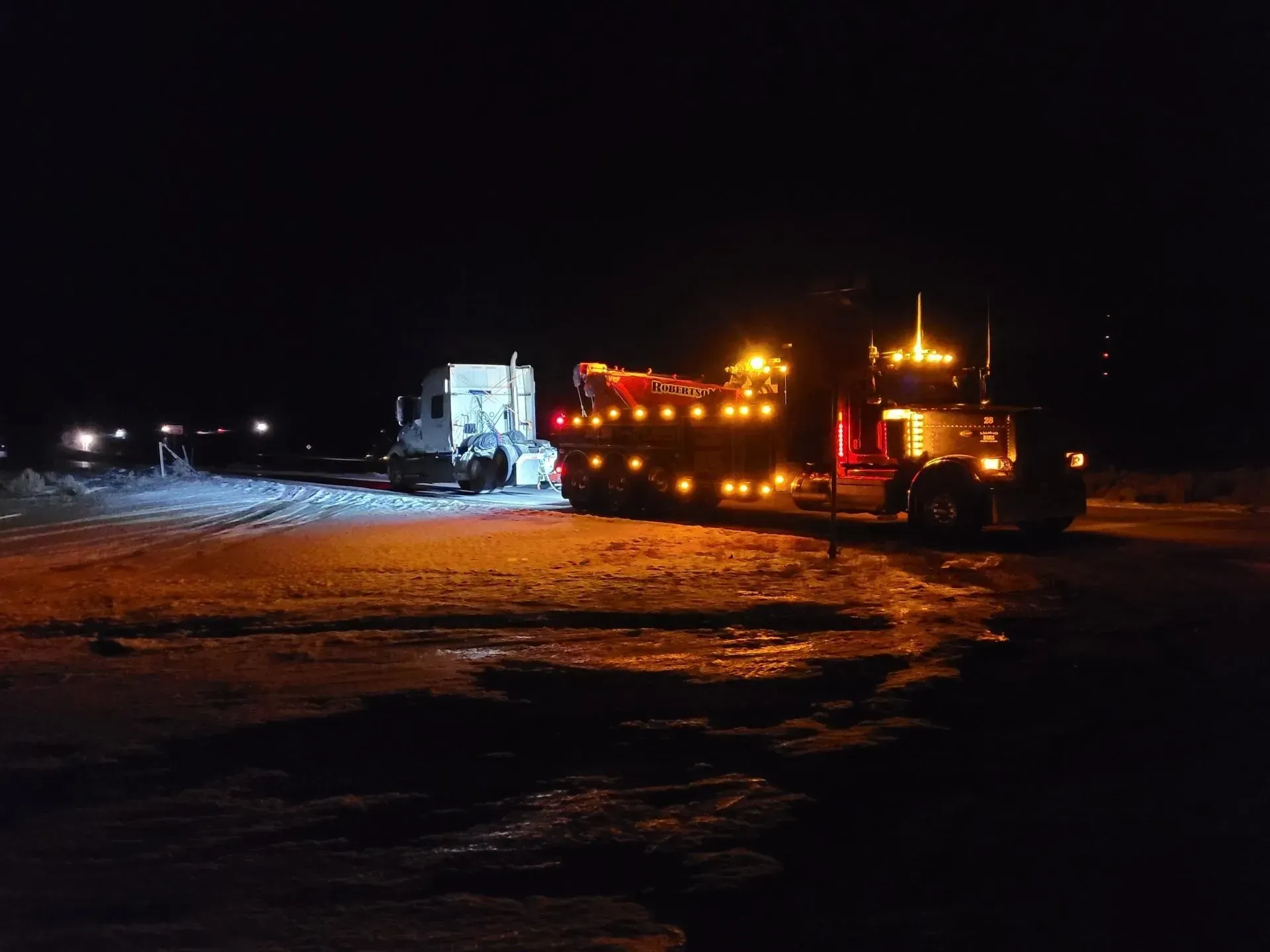 A tow truck is towing a semi truck in the snow at night — Evanston, WY — Robertson Transportation Inc. Towing and Recovery