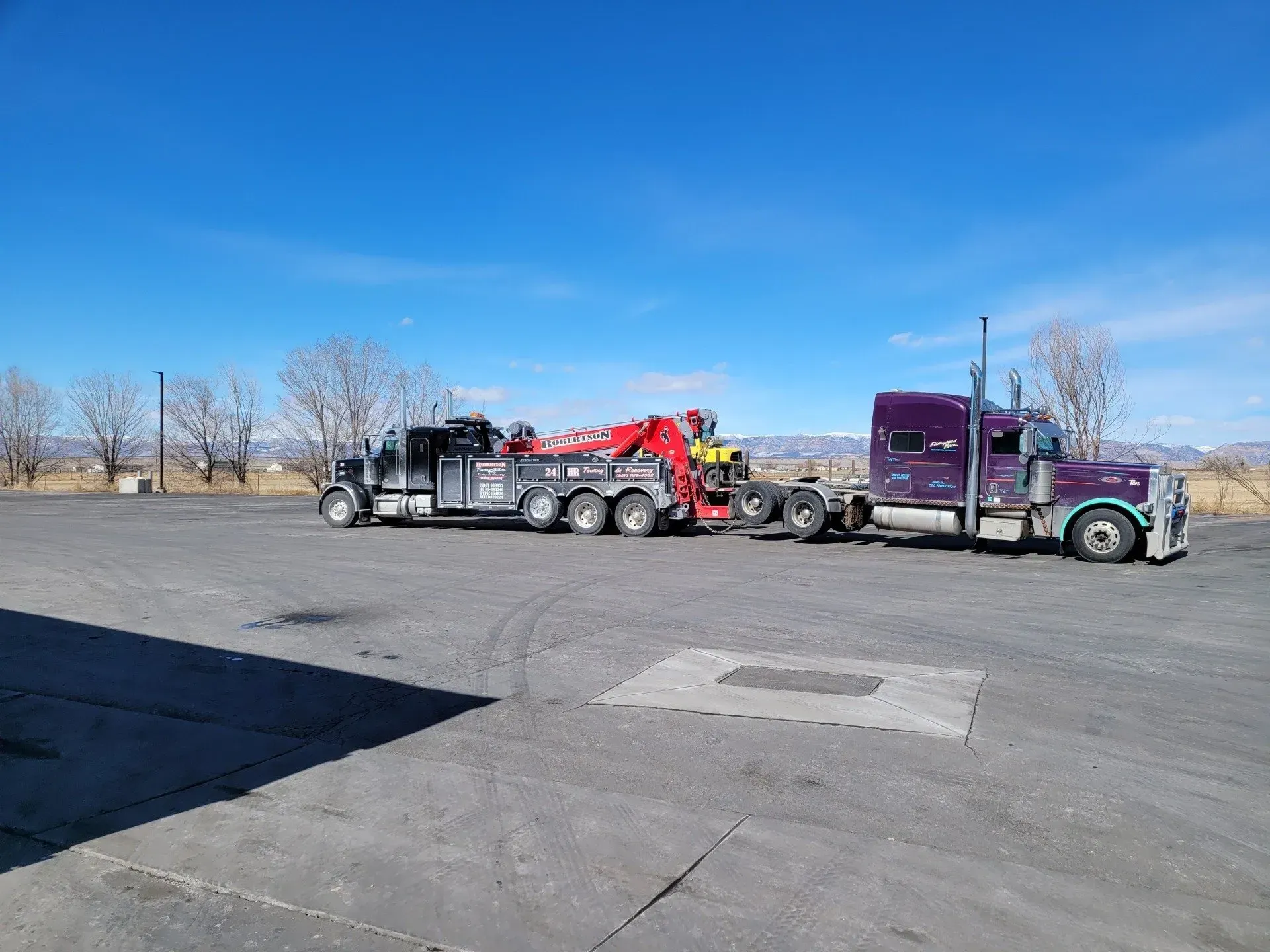 A purple tow truck is towing a black truck in a parking lot — Evanston, WY — Robertson Transportation Inc. Towing and Recovery
