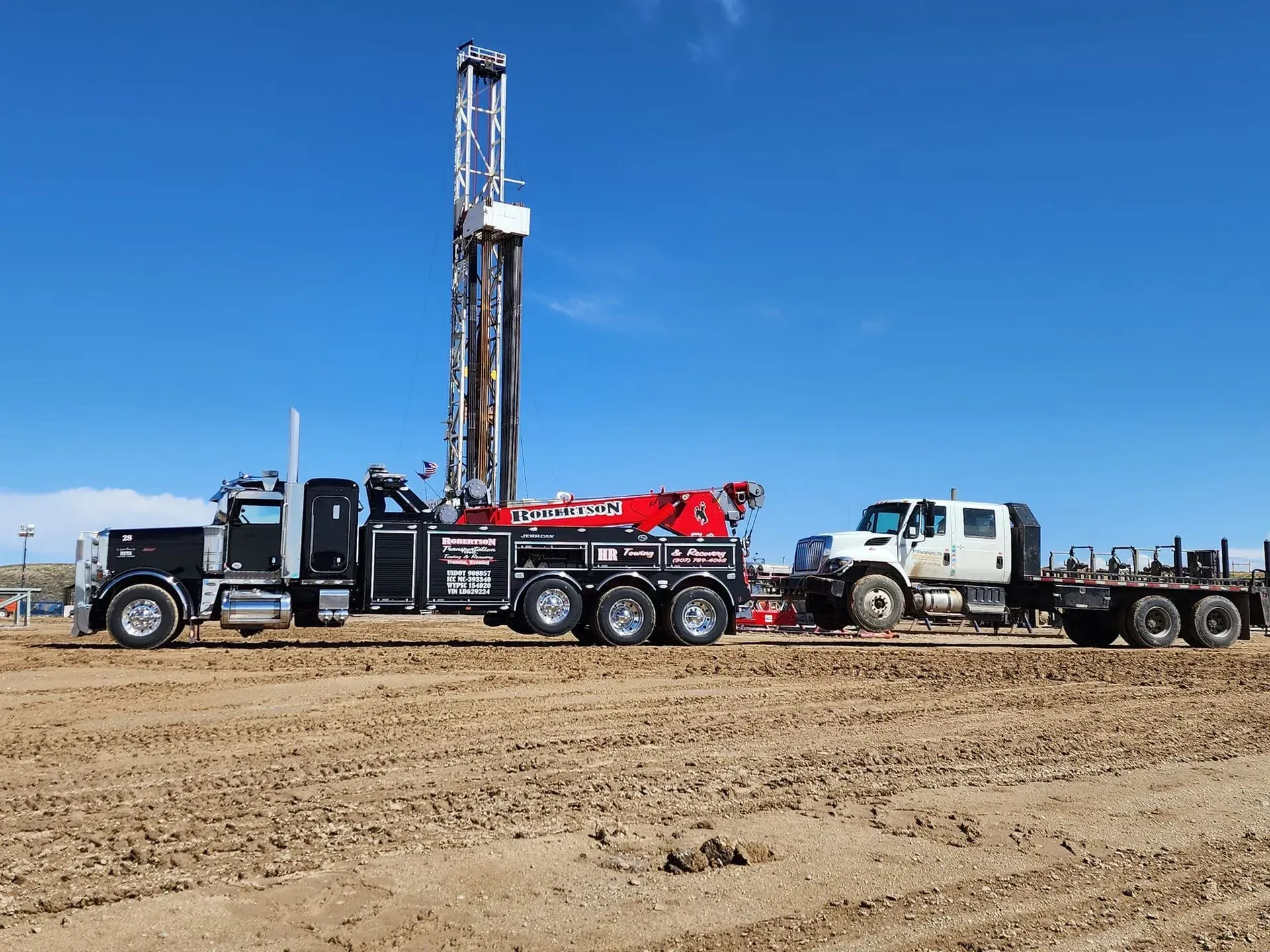 A truck is towing a drilling rig in a dirt field — Evanston, WY — Robertson Transportation Inc. Towing and Recovery