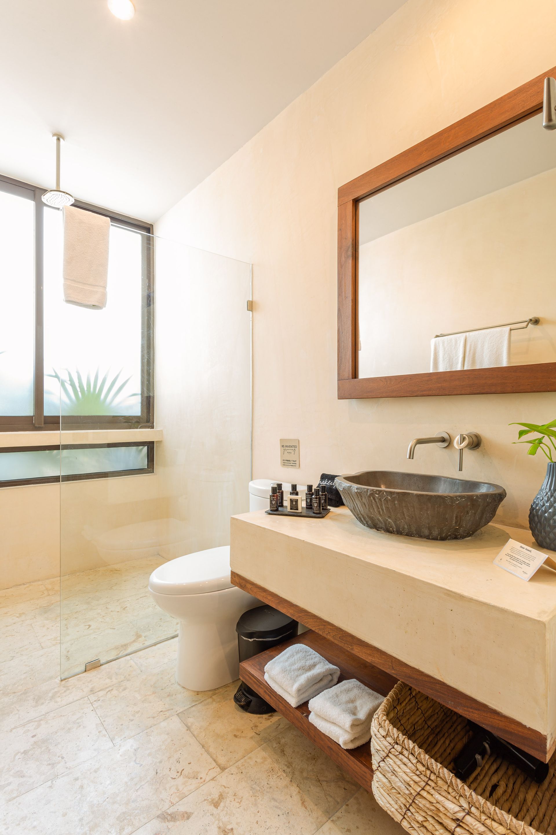A bathroom with a toilet , sink , mirror and window.