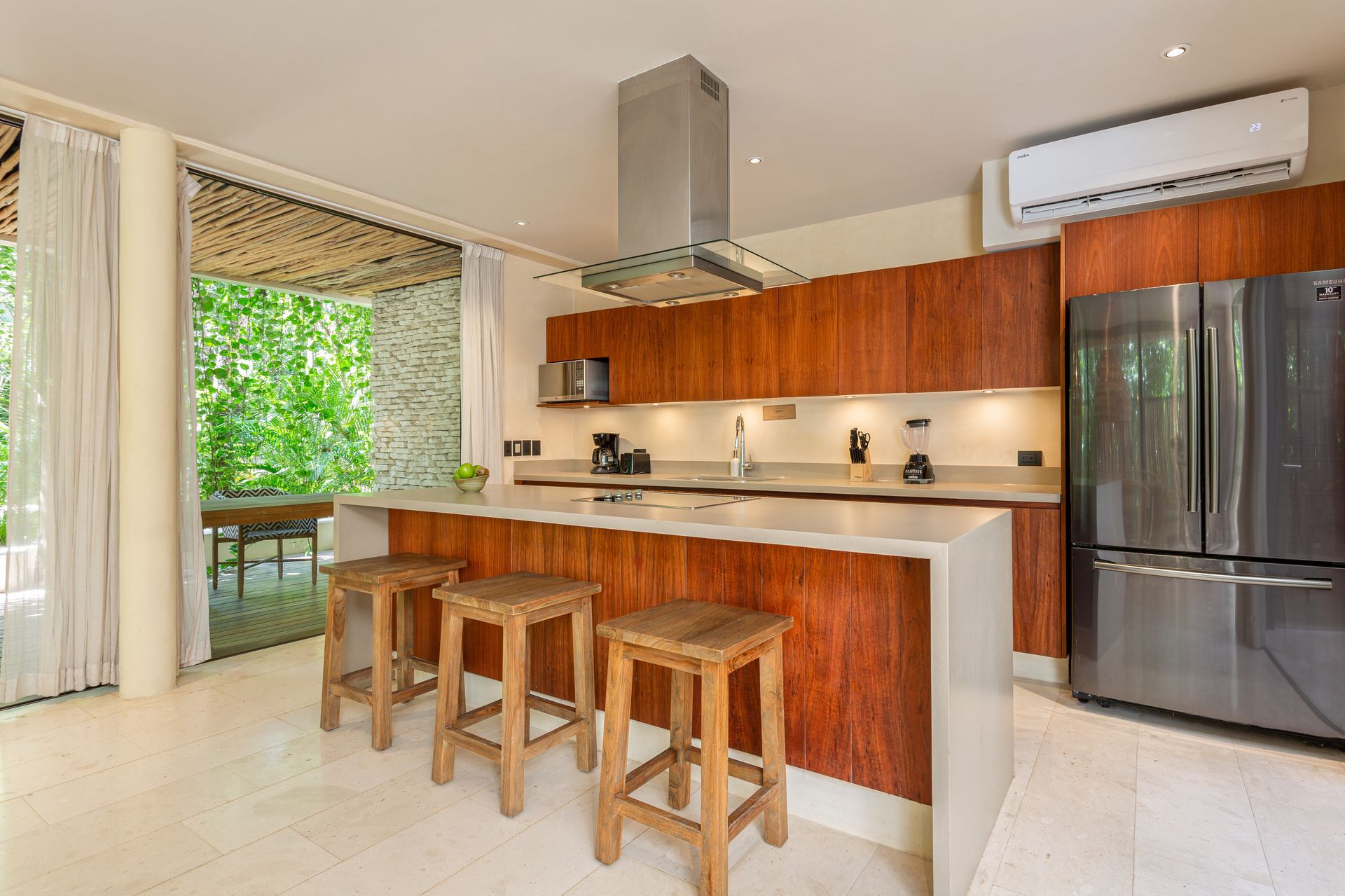A kitchen with wooden cabinets and stools and a stainless steel refrigerator