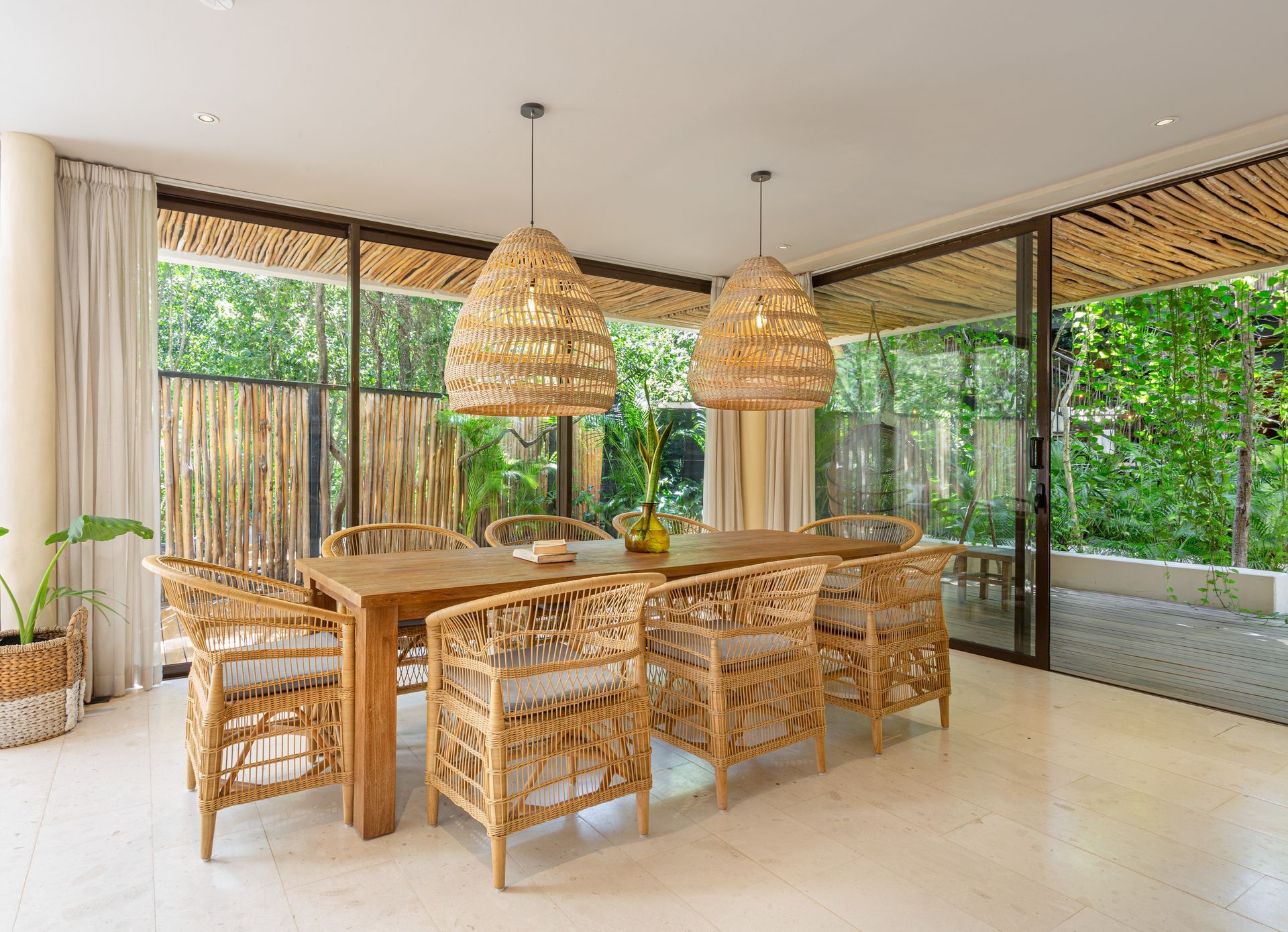 A dining room with a long wooden table and wicker chairs.