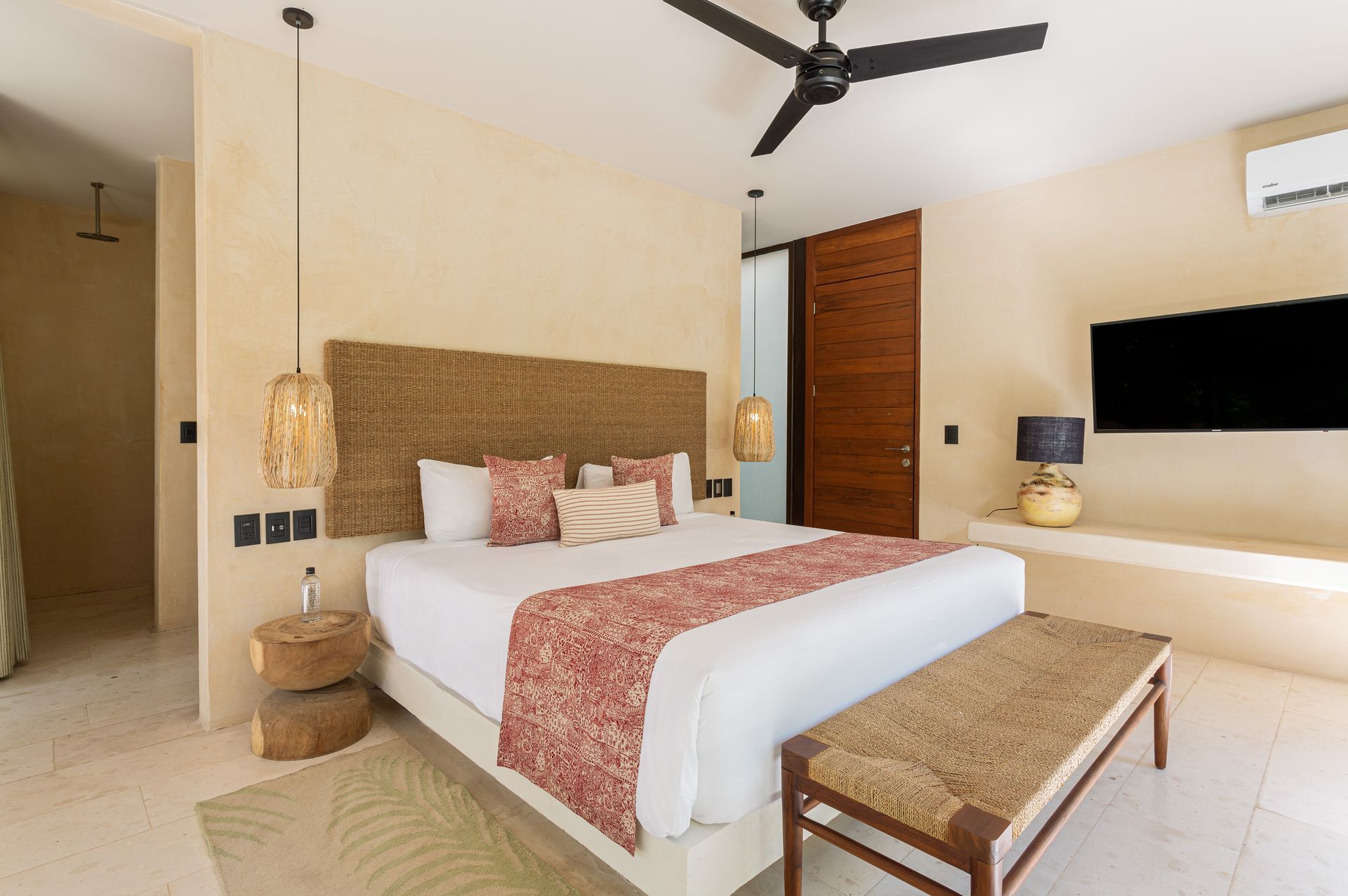 A hotel room with a large bed , ceiling fan , television and a bench.
