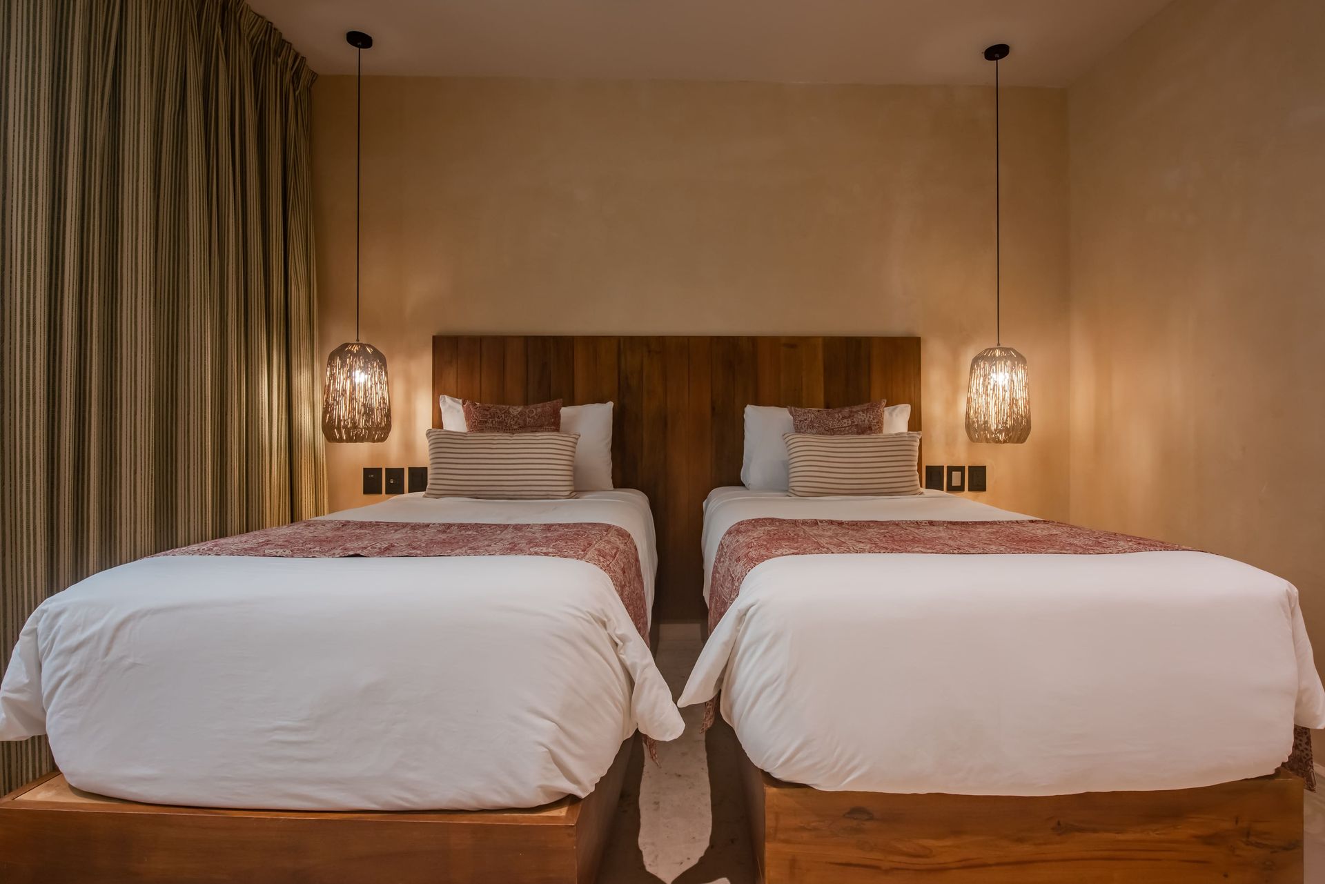 A hotel room with two beds and two lamps hanging from the ceiling.