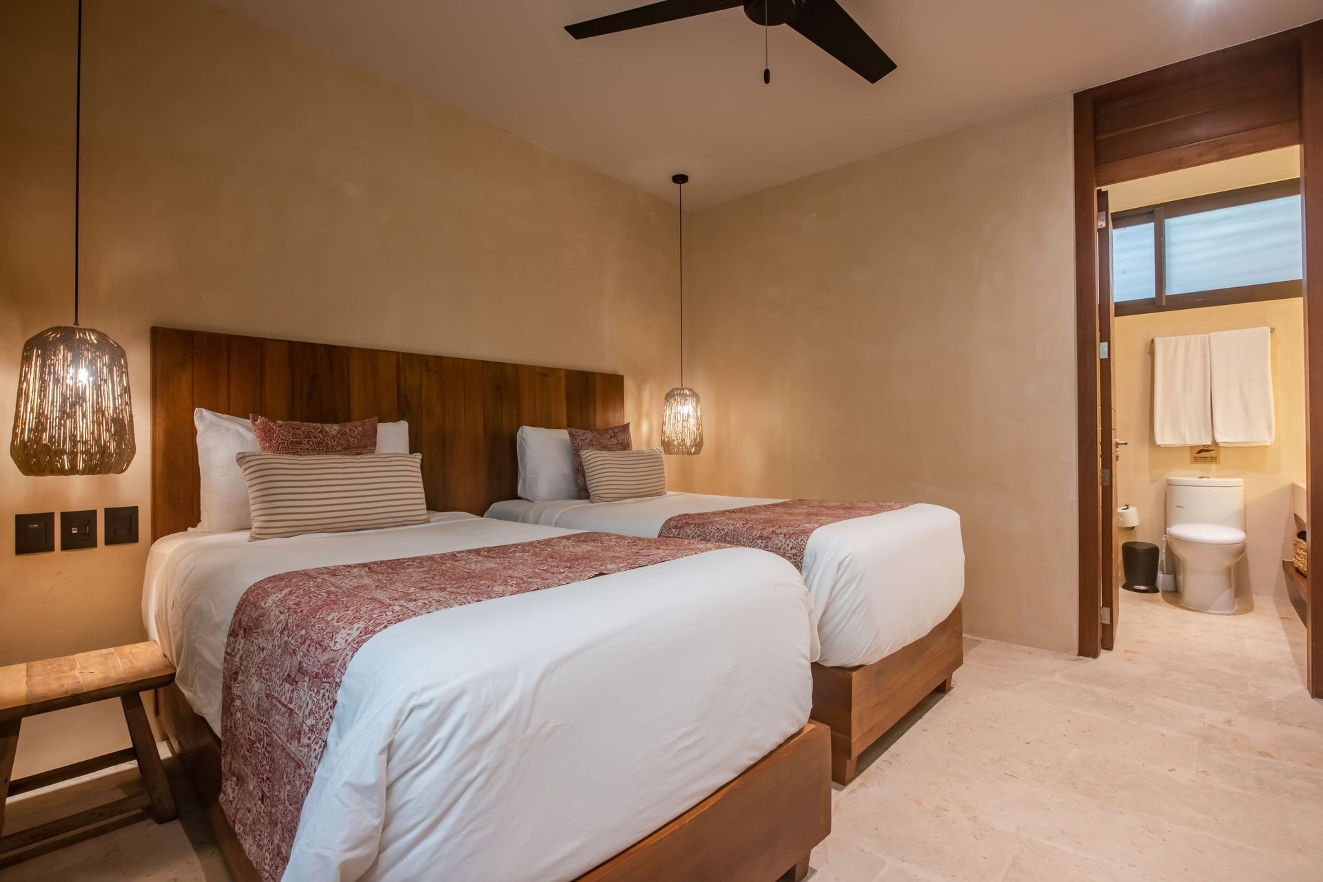 A hotel room with two beds , a toilet and a ceiling fan.