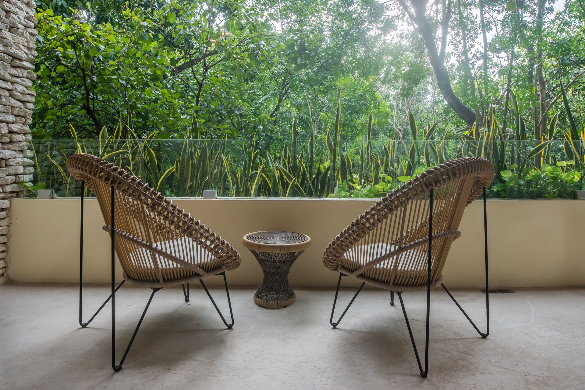 Two wicker chairs and a table on a balcony with trees in the background.