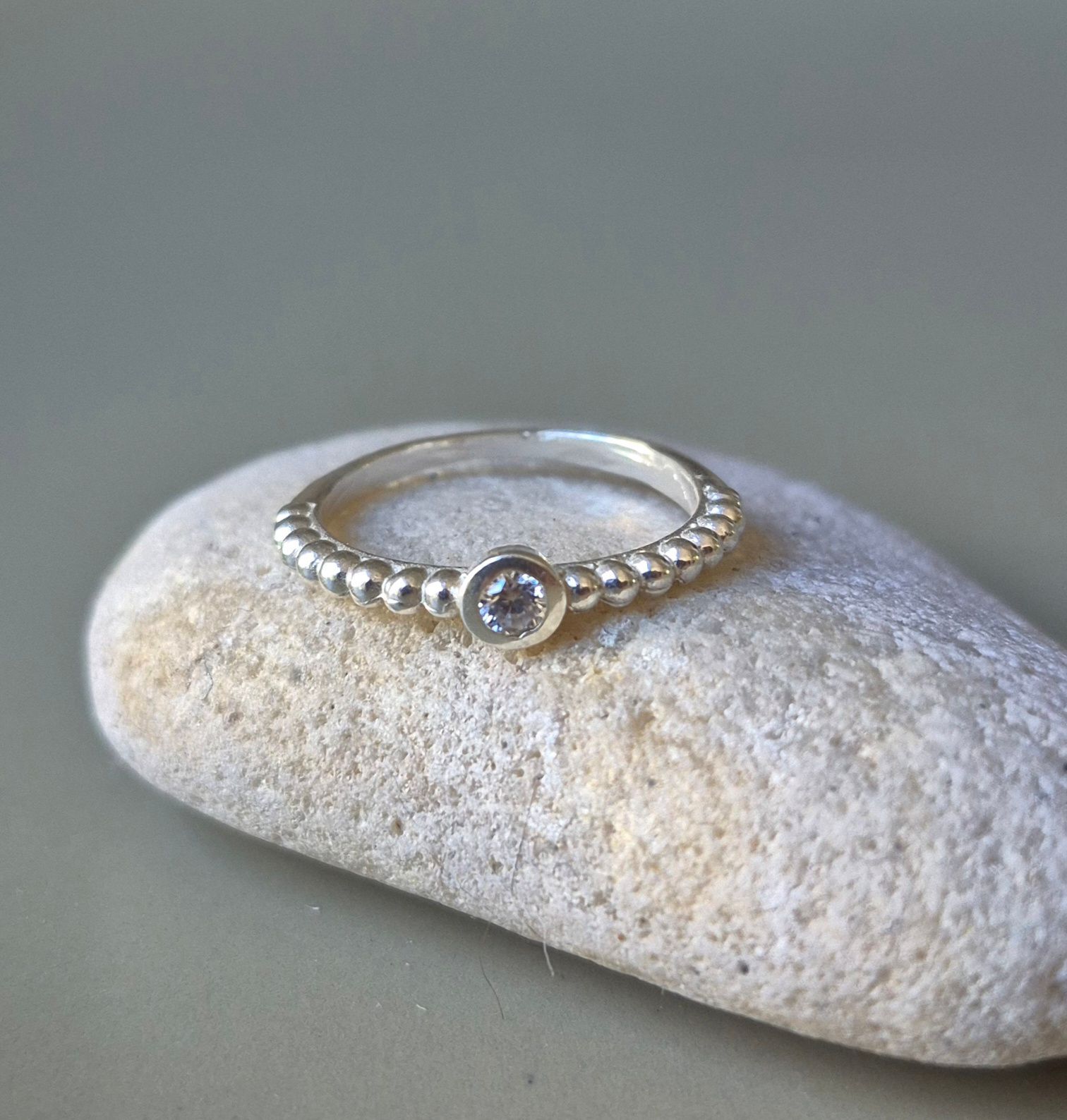 Anillo de plata con una pequeña gema, que reposa sobre una piedra gris claro.