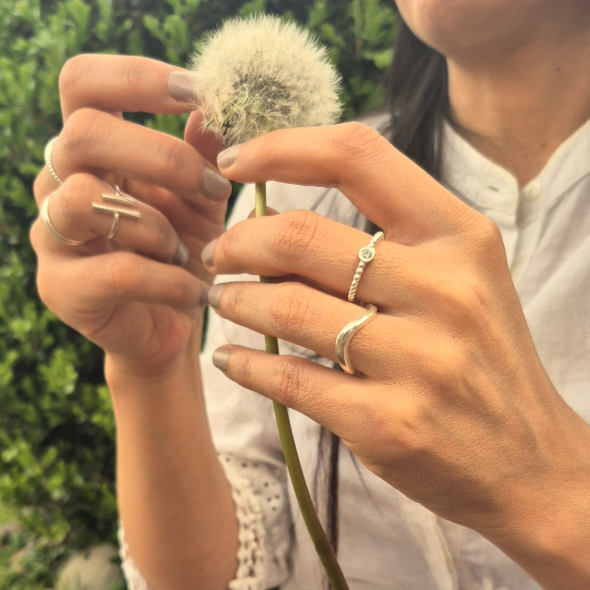 Mujer sosteniendo un diente de león, adornado con anillos en sus dedos, al aire libre.