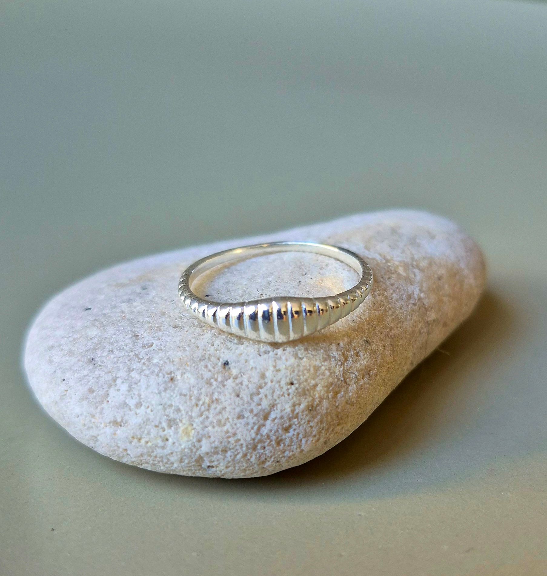 Anillo de plata con diseño acanalado sobre piedra blanca texturizada.
