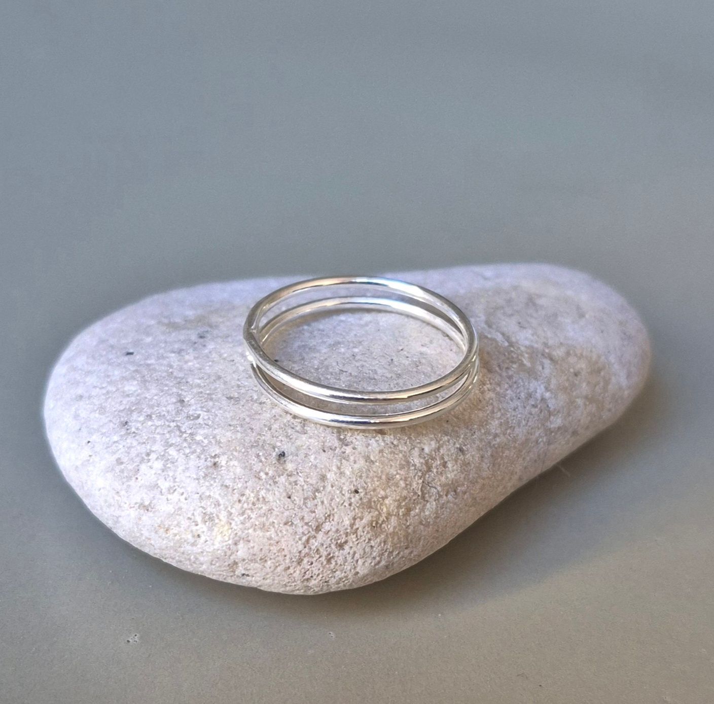 Anillo de plata de doble banda sobre una pequeña roca gris texturizada.