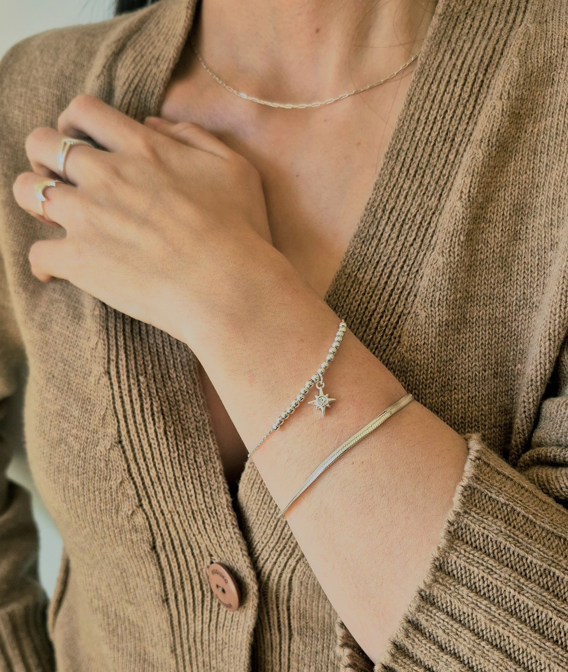 Mujer con un cárdigan marrón y joyas, incluido un collar, anillos y dos pulseras con un dije de estrella.