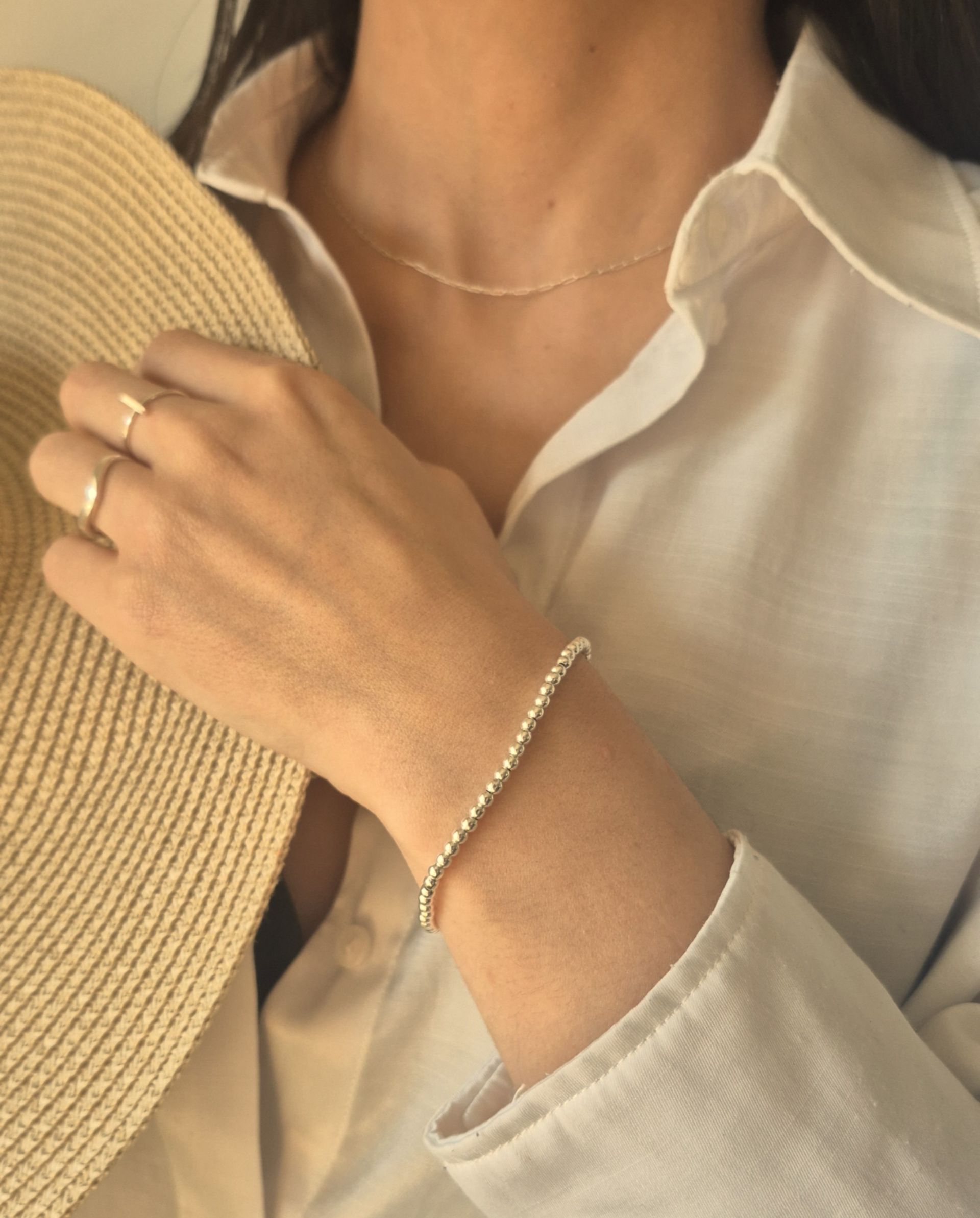 Mujer que lleva un collar y una pulsera, sosteniendo un sombrero para el sol.