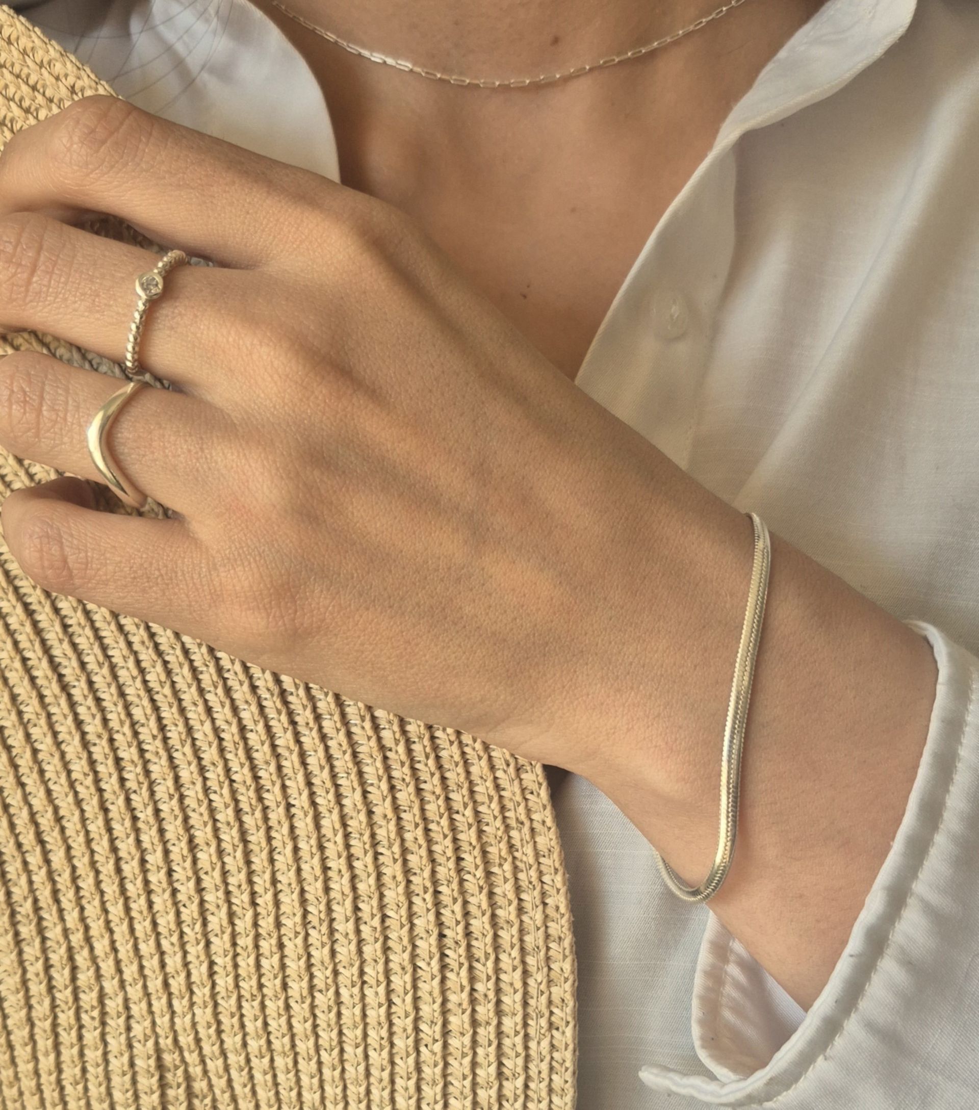 Mano de mujer con anillos y pulsera de plata, camisa blanca, sombrero de paja parcialmente visible.
