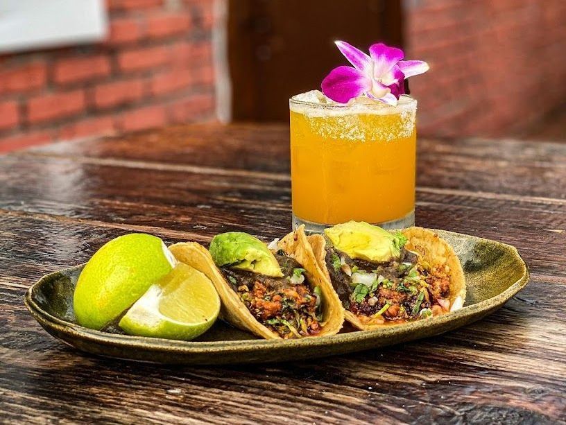 A plate of tacos and a drink on a wooden table.