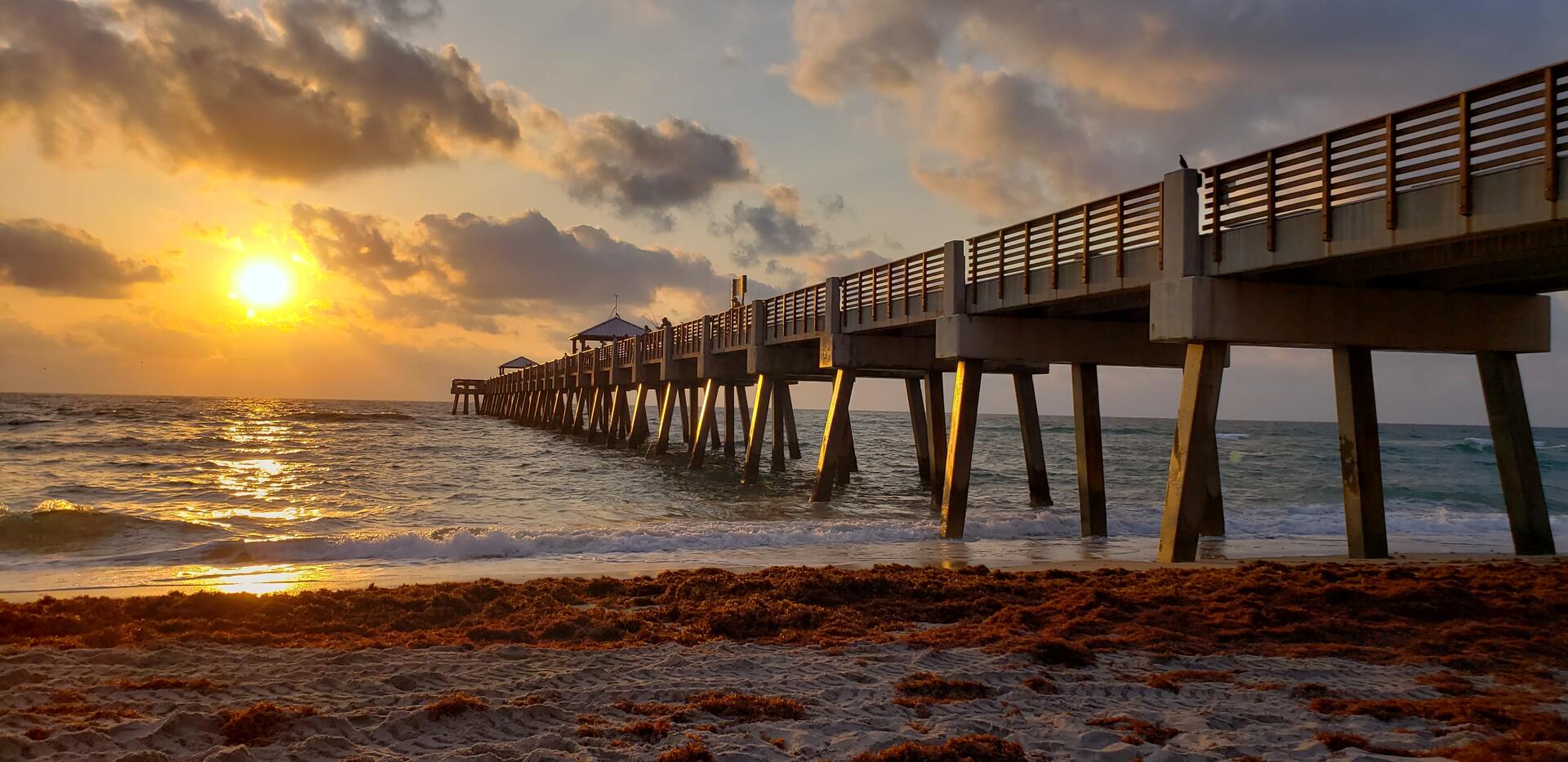 A pier overlooking the ocean at sunset with the sun shining through the clouds.