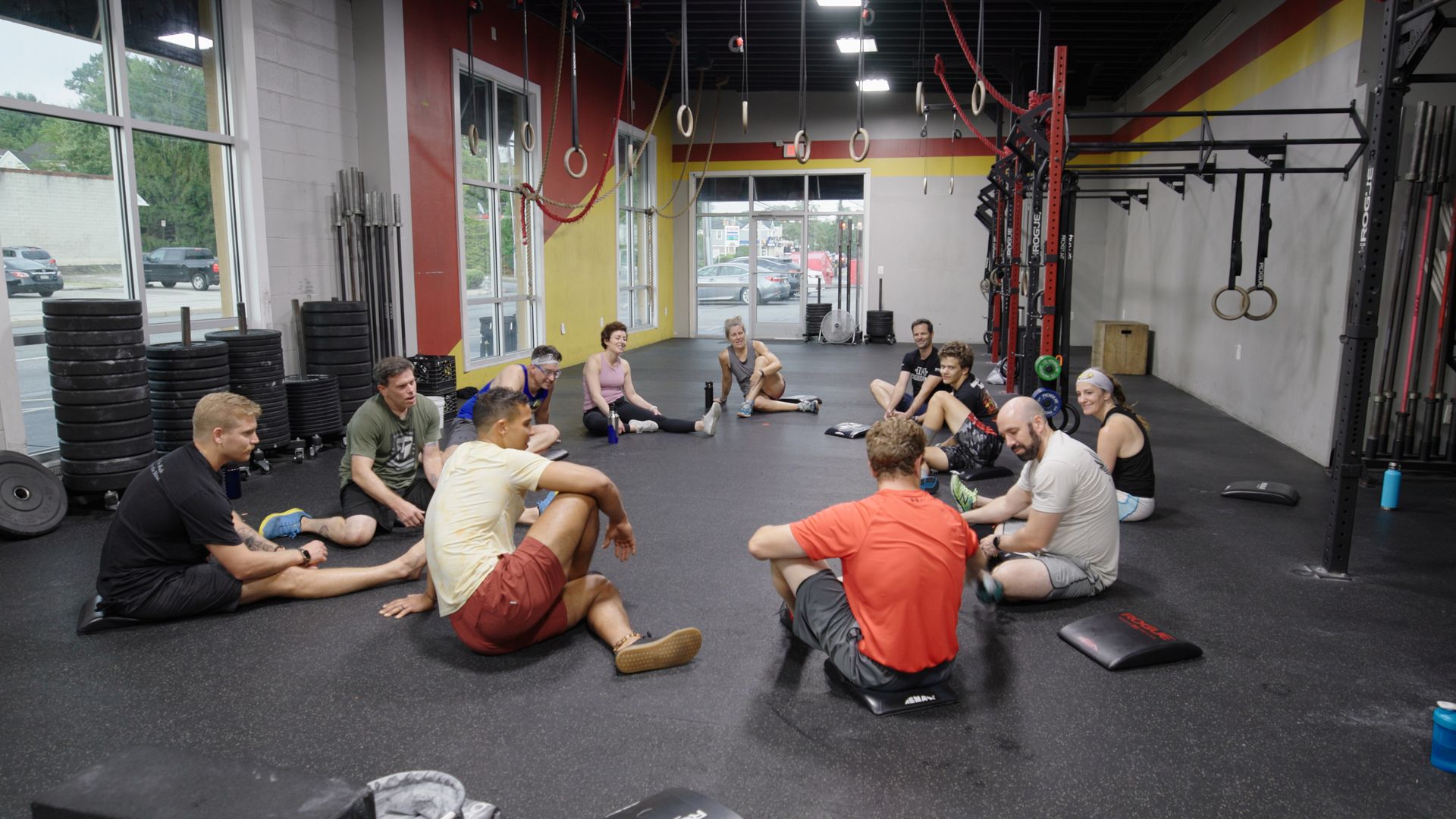 A group of people are sitting in a circle on the floor in a gym.