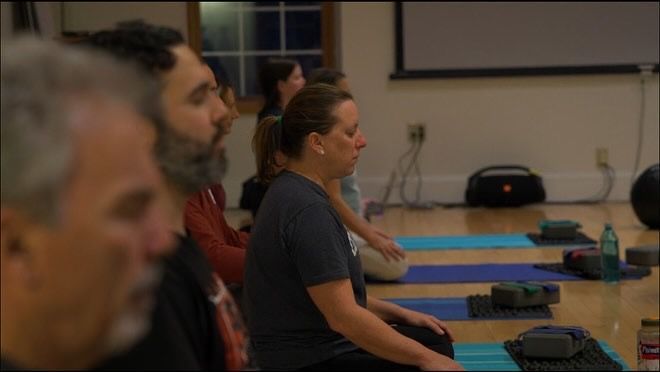 A group of people are sitting on yoga mats in a room
