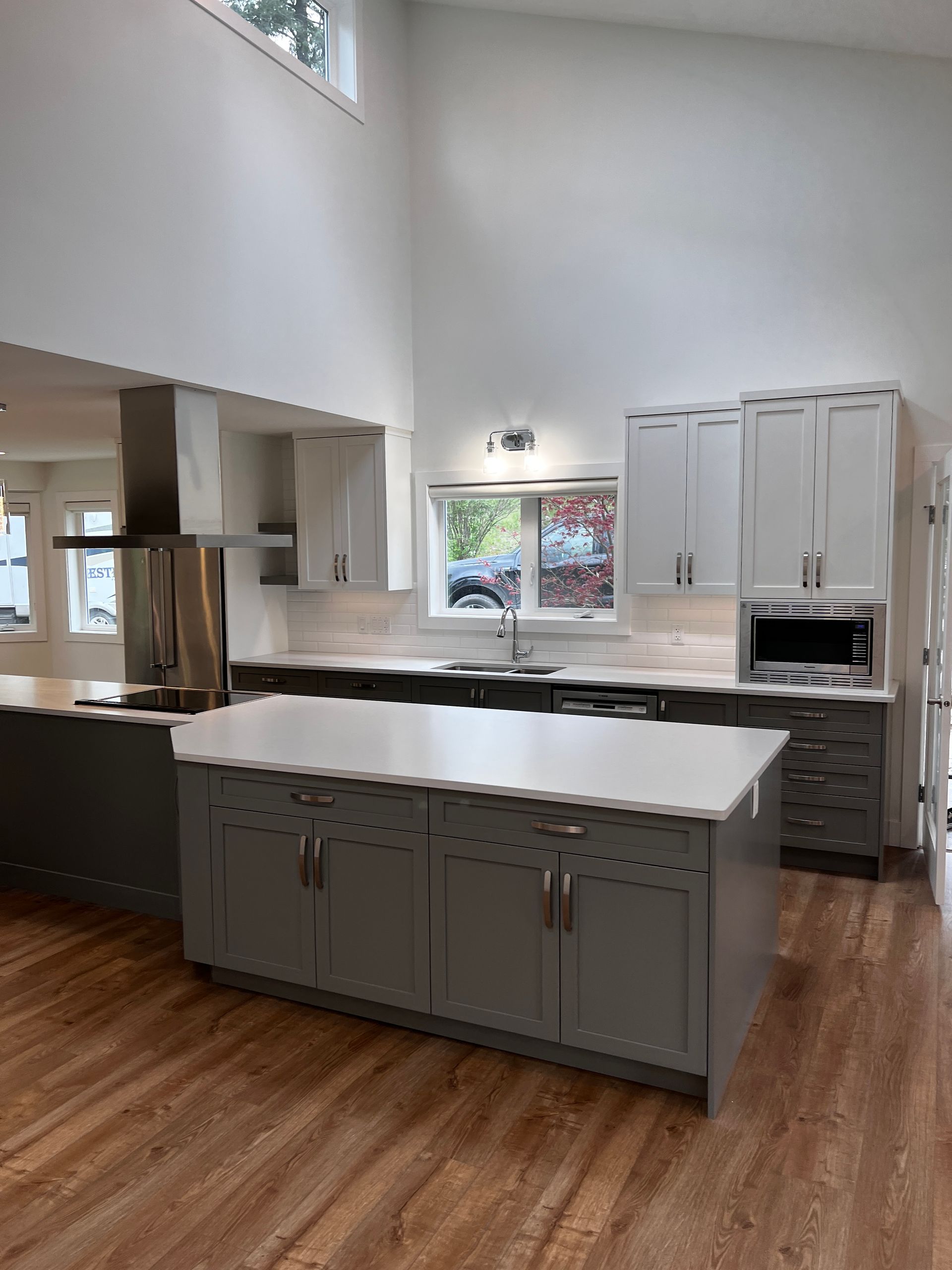 Kitchen with Dark Grey cabinets and white quartz countertop, stainless steel fridge, range hood and microwave. Chrome faucet