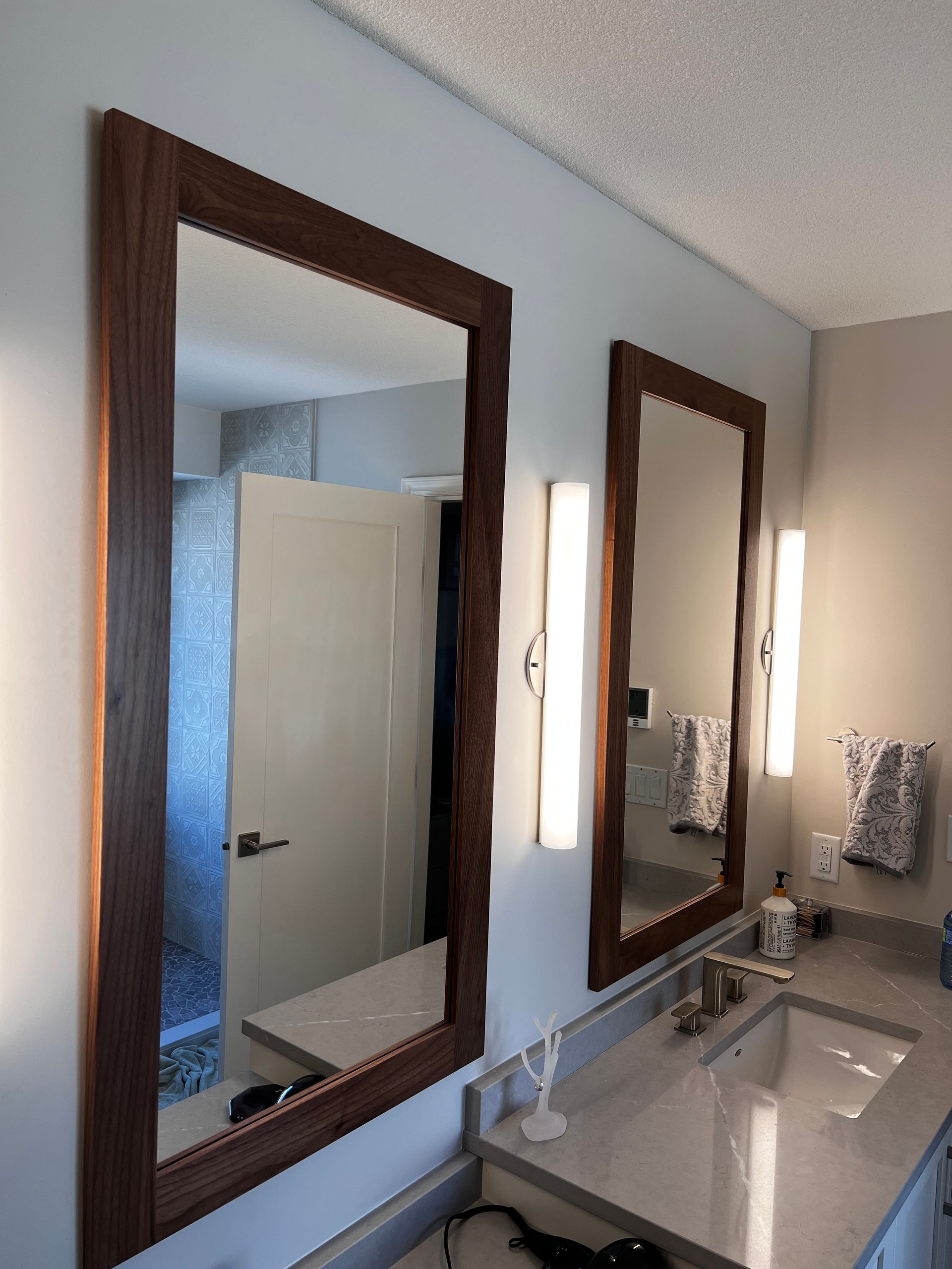 Wood-framed mirrors in a bathroom with wall sconce lighting fixtures.