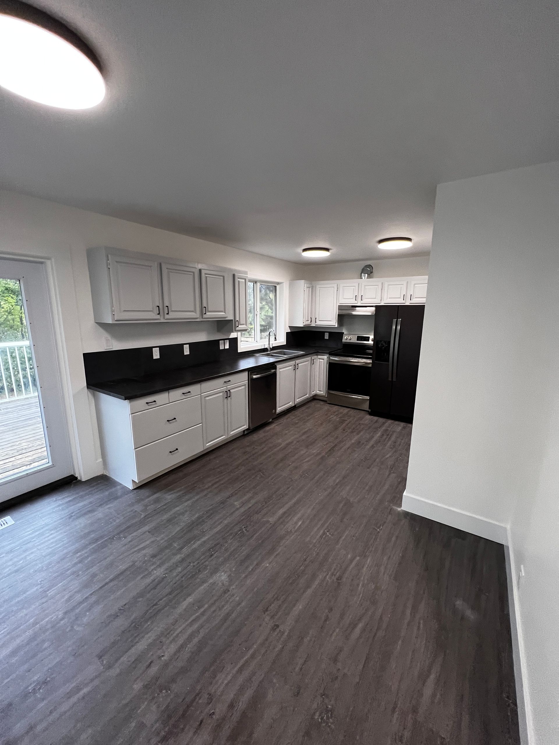 Kitchen with light grey cabinets, black laminate countertop, dark grey vinyl flooring, patio door and white walls.