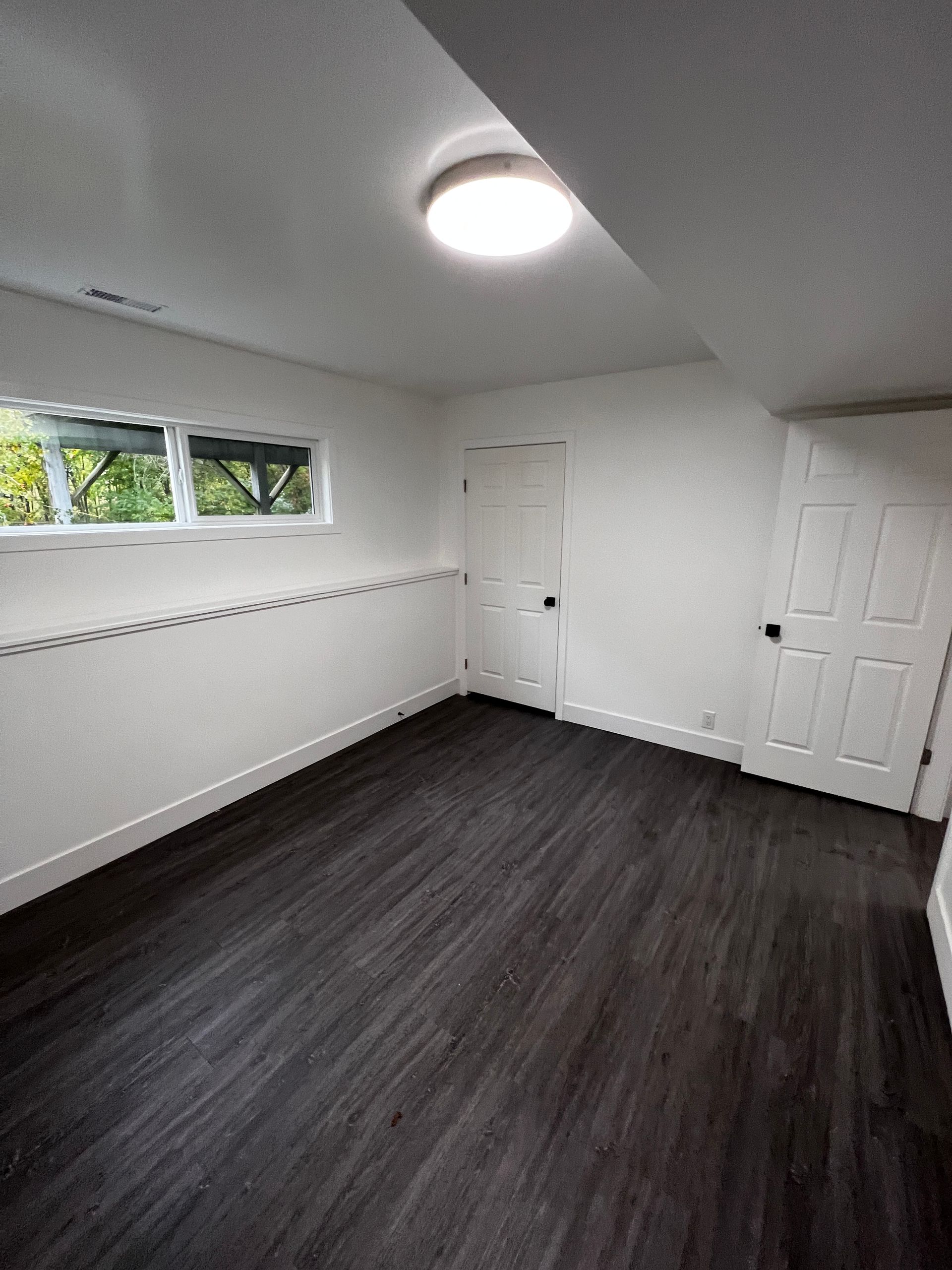 basement suite with dark grey flooring, white walls, interior doors, baseboard and basement window.